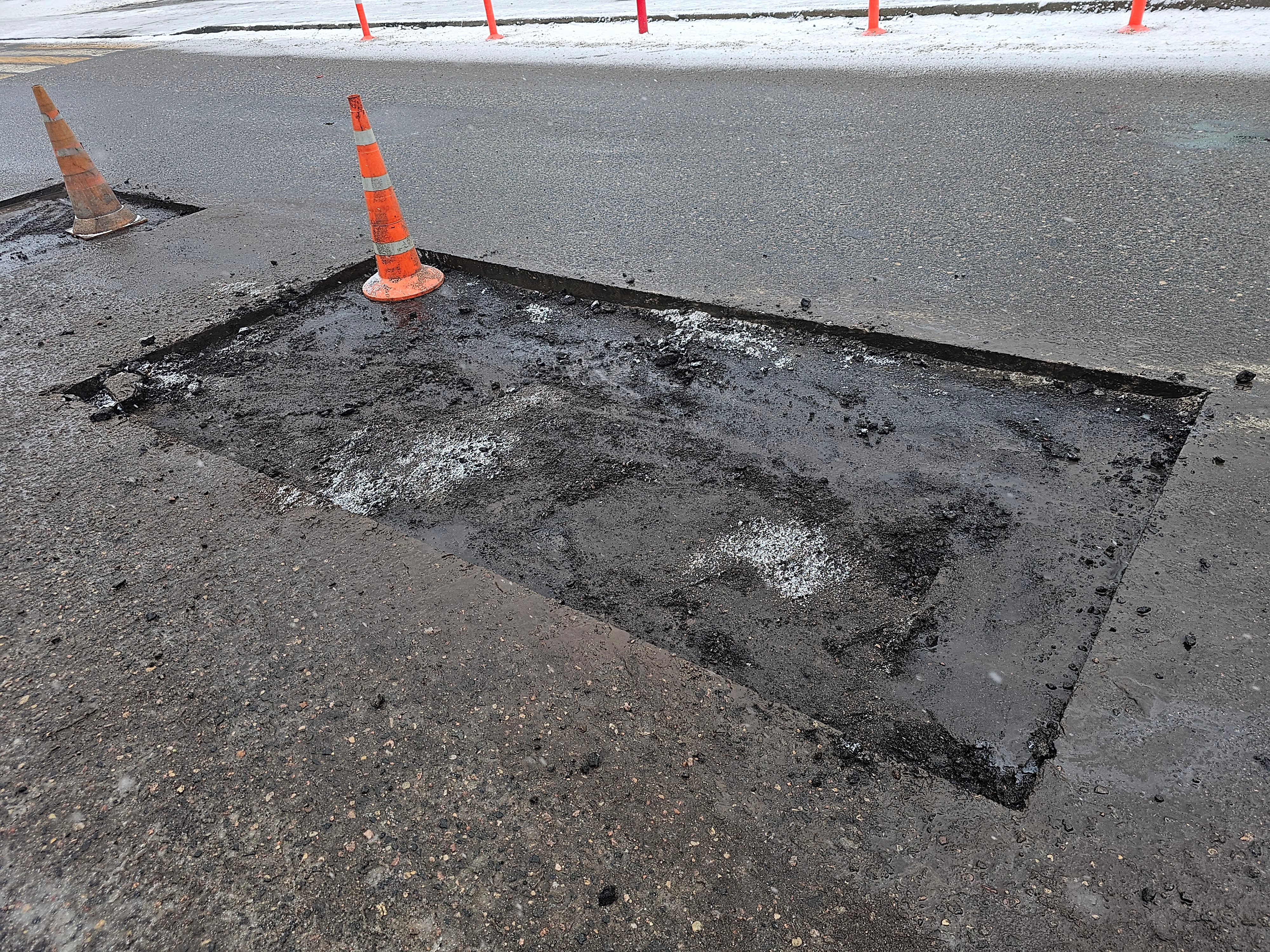 Pothole repair efforts underway on busy road with construction cones marking hazardous area